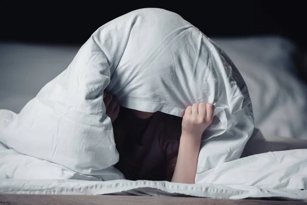 Niño asustado escondido bajo manta aislado en negro - foto de stock