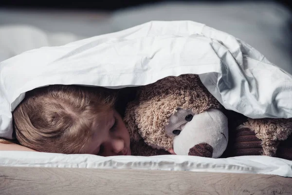Verängstigtes Kind liegt unter Decke in der Nähe von Teddybär isoliert auf schwarz — Stockfoto