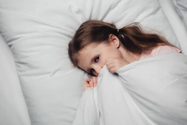 Vista dall'alto di bambino spaventato sdraiato su biancheria da letto bianca e guardando la fotocamera — Foto stock