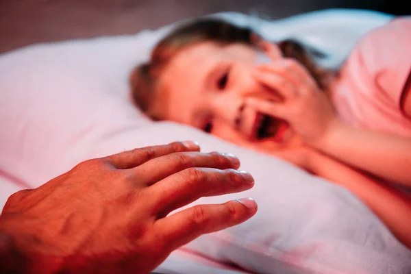 Selective focus of male hand near scared, screaming child lying in bed — Stock Photo