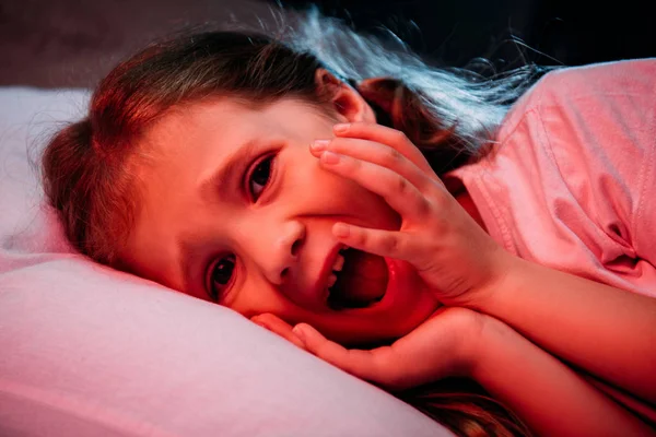 Frightened child screaming and looking at camera while lying in dark bedroom — Stock Photo