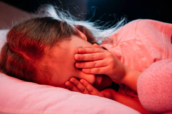 Bambino spaventato che copre gli occhi con le mani mentre si trova a letto isolato su nero — Foto stock