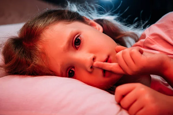 Bambino spaventato sdraiato in camera da letto buia, mostrando il segno del silenzio e guardando la fotocamera — Foto stock