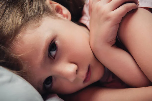 Niedliches, verängstigtes Kind, das im dunklen Schlafzimmer in die Kamera schaut — Stockfoto