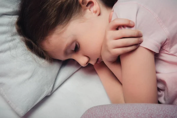 Adorable frightened child lying on white bedding and embracing herself with arms — Stock Photo