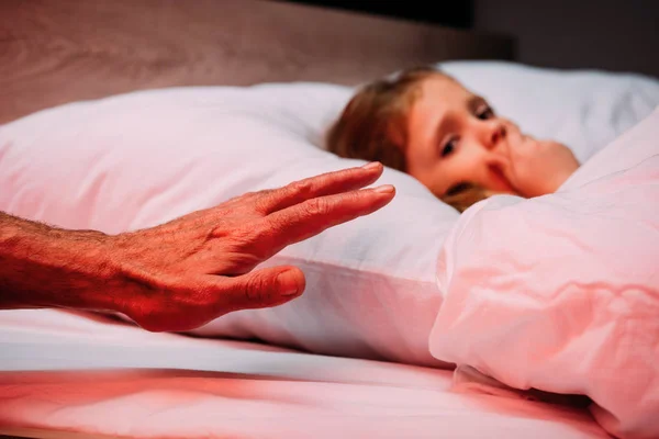 Mano maschile vicino spaventato bambino sdraiato a letto e mostrando segno di silenzio — Foto stock