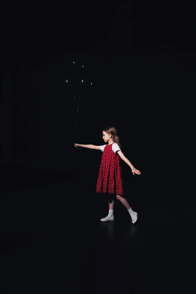 Lonely child walking with black balloons isolated on black — Stock Photo