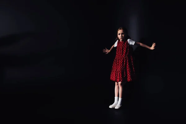 Asustado, niño solitario mirando a la cámara mientras está de pie sobre fondo negro - foto de stock