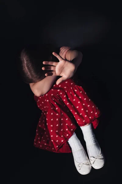 Испуганный, одинокий ребенок сидит с протянутой рукой на черном фоне — стоковое фото