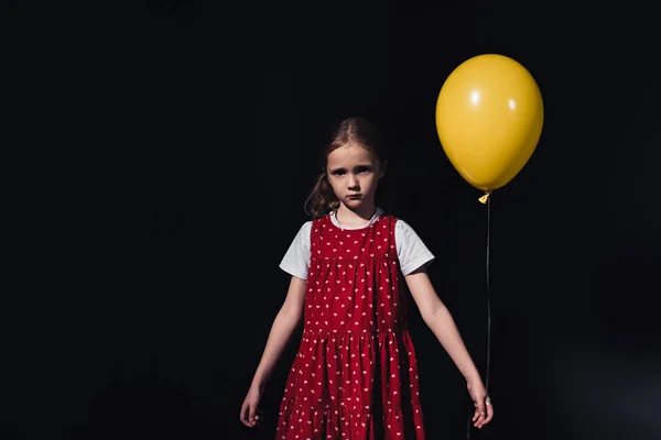 Offended, lonely child with yellow balloon looking at camera isolated on black — Stock Photo