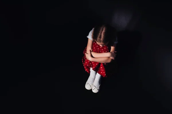 Vista aérea del niño deprimido sentado en el suelo sobre fondo negro - foto de stock