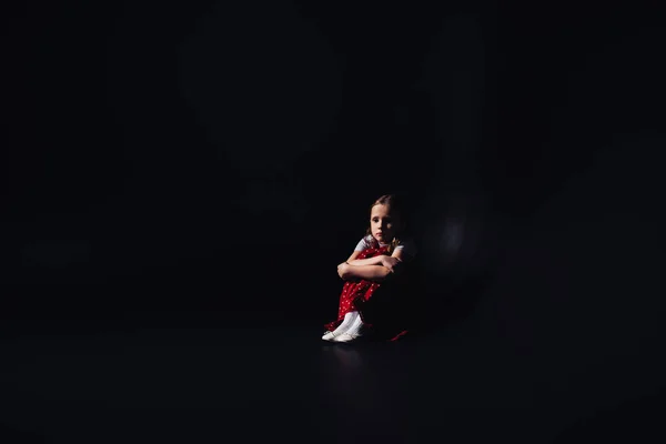 Verängstigtes, einsames Kind auf dem Boden sitzend auf schwarzem Hintergrund mit Kopierraum — Stockfoto
