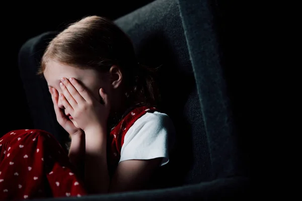 Deprimido, niño asustado cubriendo la cara con las manos aisladas en negro - foto de stock