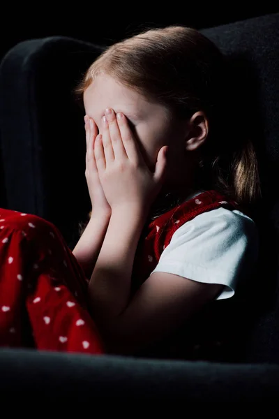 Испуганный ребенок закрывает лицо руками, изолированными на черном — стоковое фото