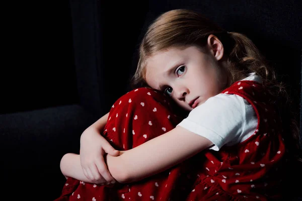 Depressed, scared child sitting and looking at camera isolated on black — Stock Photo