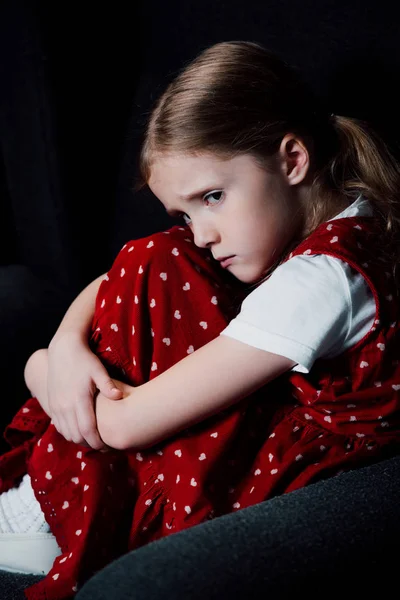 Offended, frightened kid sitting in armchair isolated on black — Stock Photo