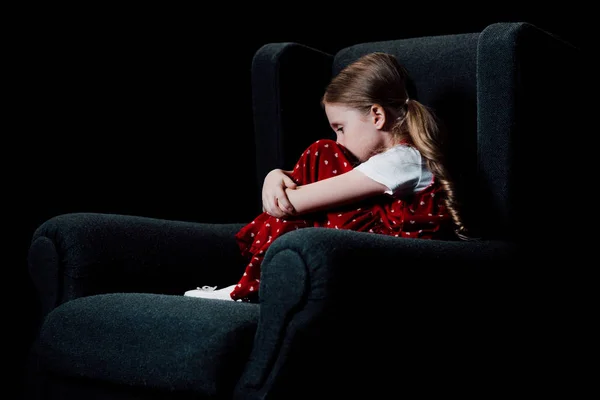 Criança assustada e solitária sentada em poltrona isolada em preto — Fotografia de Stock