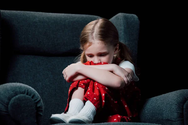 Criança sozinha, assustada sentada em poltrona isolada em preto — Fotografia de Stock