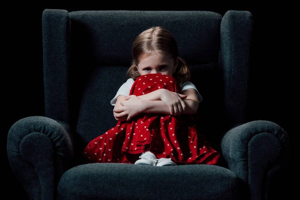 Einsames, verängstigtes Kind, das im Sessel sitzt und isoliert auf schwarz in die Kamera schaut — Stockfoto