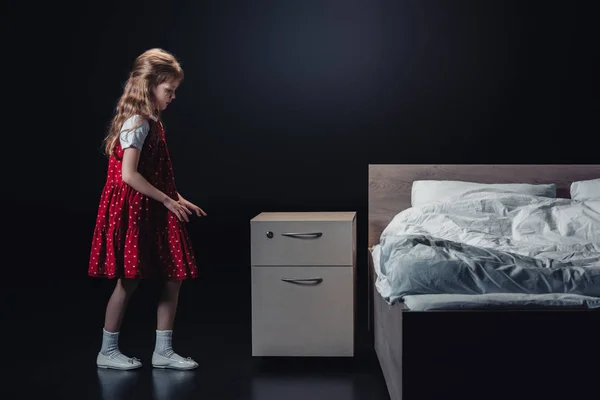 Adorabile bambino in piedi vicino comodino su sfondo nero — Foto stock