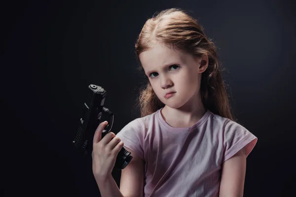 Beleidigtes Kind mit Waffe und Blick auf Kamera isoliert auf schwarz — Stockfoto