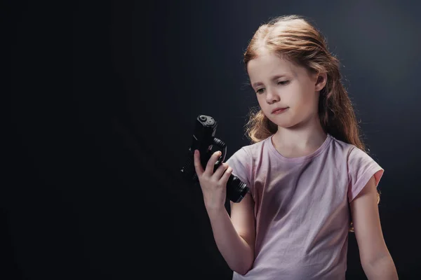 Niño ofendido mirando arma en mano sobre fondo negro - foto de stock