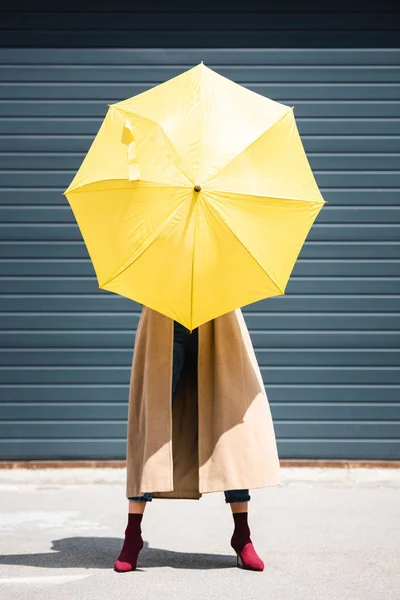 Jeune femme adulte en manteau tenant parapluie jaune à l'extérieur — Photo de stock