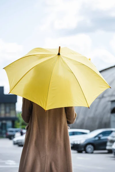 Vue arrière de la femme en manteau tenant parapluie jaune — Photo de stock