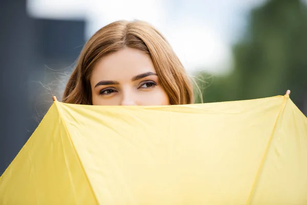 Vista recortada de mujer atractiva con paraguas amarillo en el exterior - foto de stock