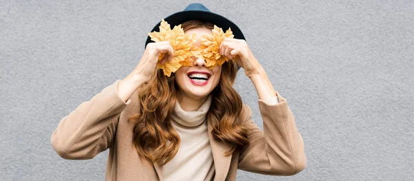 Panoramic shot of woman in blue hat smiling and holding yellow leaves — Stock Photo