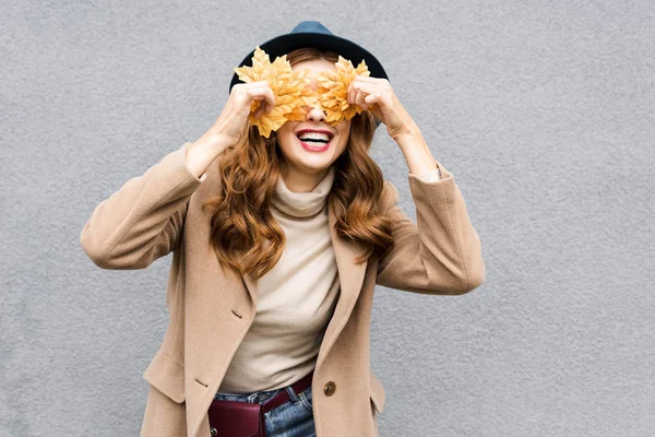 Mulher de chapéu azul sorrindo e segurando folhas amarelas — Fotografia de Stock