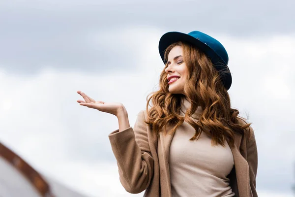 Attraktive und lächelnde Frau mit blauem Hut und geschlossenen Augen — Stockfoto