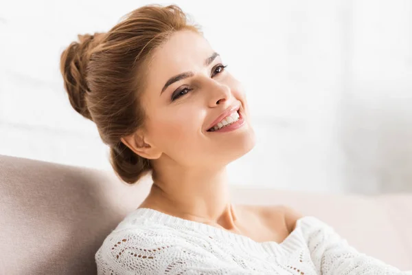 Atractiva mujer en suéter blanco sonriendo y mirando hacia otro lado - foto de stock