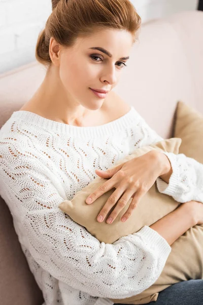 Attraktive Frau im weißen Pullover mit Kopfkissen und wegschauendem Blick — Stockfoto