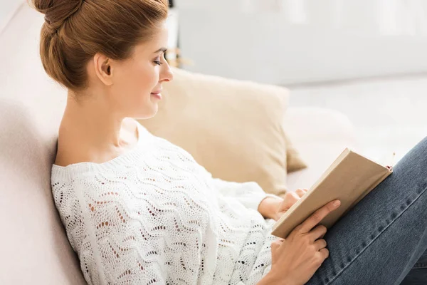 Side view of attractive woman in white sweater reading book — Stock Photo