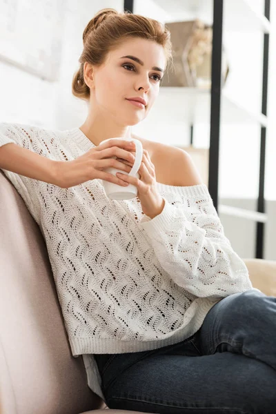 Attractive woman in white sweater holding cap and looking away — Stock Photo