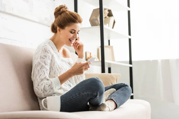 Atractiva mujer en suéter blanco sonriendo y usando teléfono inteligente - foto de stock