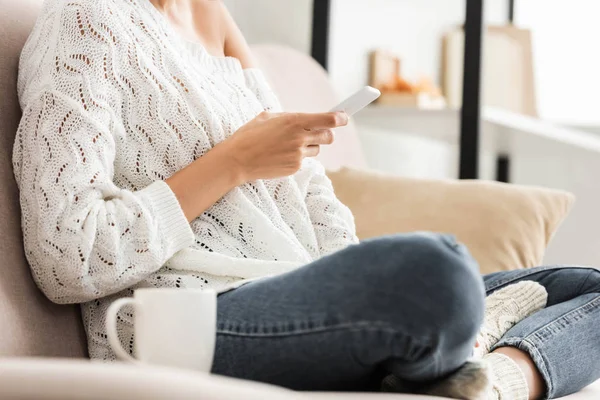 Cropped view of woman in white sweater and jeans using smartphone — Stock Photo