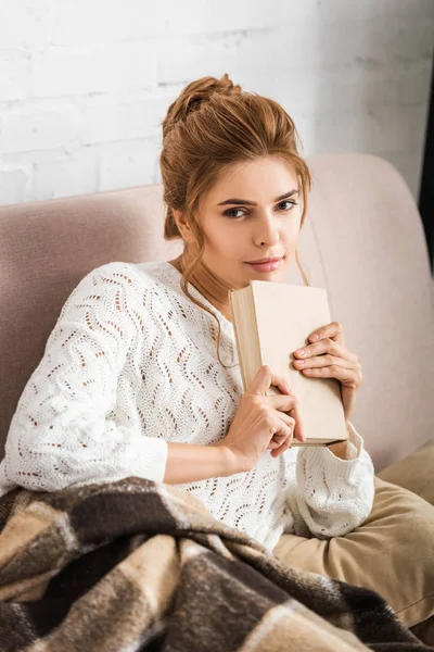 Mulher atraente em camisola branca segurando livro e olhando para a câmera — Fotografia de Stock