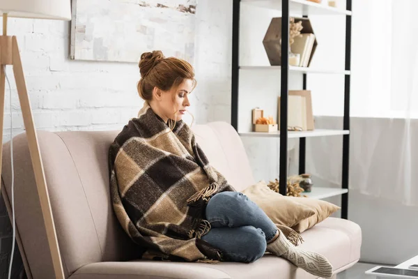 Mulher atraente com cobertor sentado no sofá no apartamento — Fotografia de Stock
