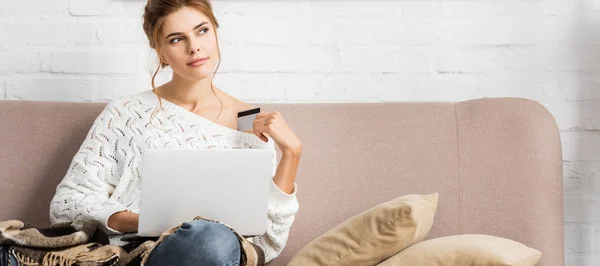 Panoramic shot of attractive woman in white sweater holding credit and laptop — Stock Photo