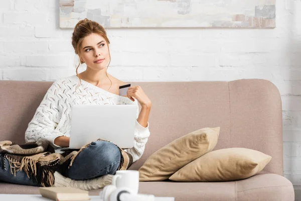 Attractive woman in white sweater holding credit and laptop — Stock Photo