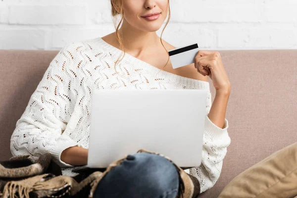 Cropped view of woman in white sweater holding credit and laptop — Stock Photo