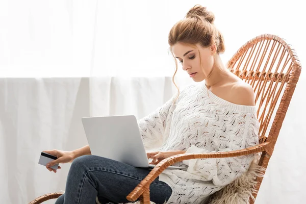 Attractive woman in white sweater holding credit and laptop — Stock Photo