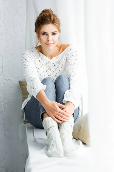 Mulher atraente em camisola branca e jeans sentado e olhando para a câmera — Fotografia de Stock