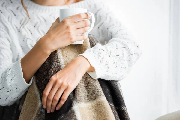 Vista cortada de mulher com cobertor em copo branco suéter segurando — Fotografia de Stock