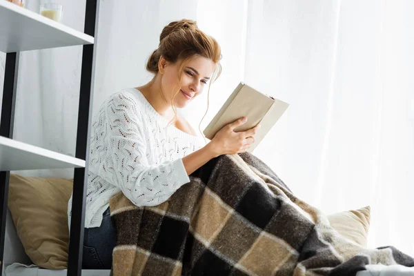 Приваблива жінка в білому светрі з книгою читання ковдрою — стокове фото