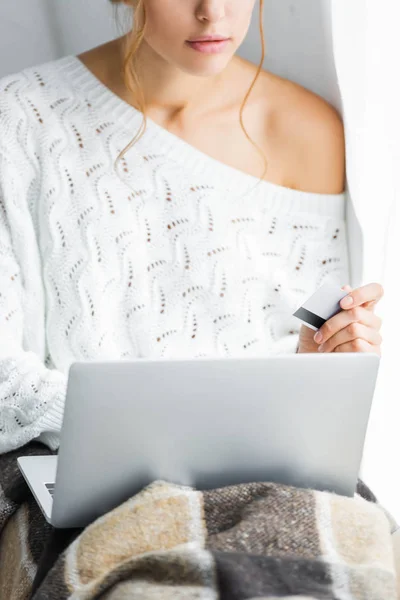 Cropped view of woman in white sweater holding credit and laptop — Stock Photo