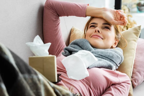 Mujer atractiva y enferma con bufanda gris acostada y mirando hacia arriba - foto de stock