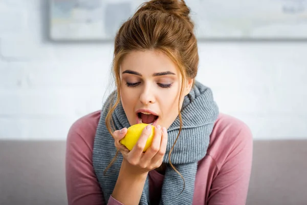 Приваблива і хвора жінка з сірим шарфом їсть жовтий лимон — стокове фото